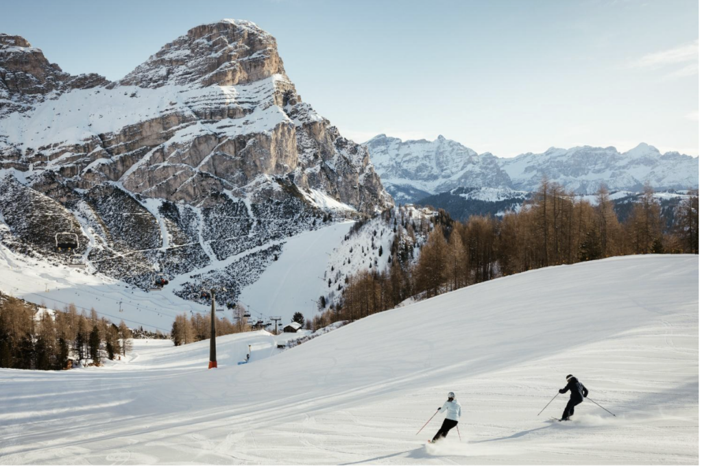 Two people are skiing down a mountain on a bluebird day in the beautiful Dolomites mountains.